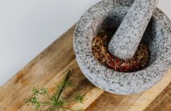 Grå mortel och mortelstöt med krossade kryddor på träbräda