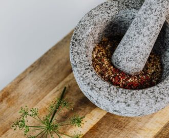 Grå mortel och mortelstöt med krossade kryddor på träbräda